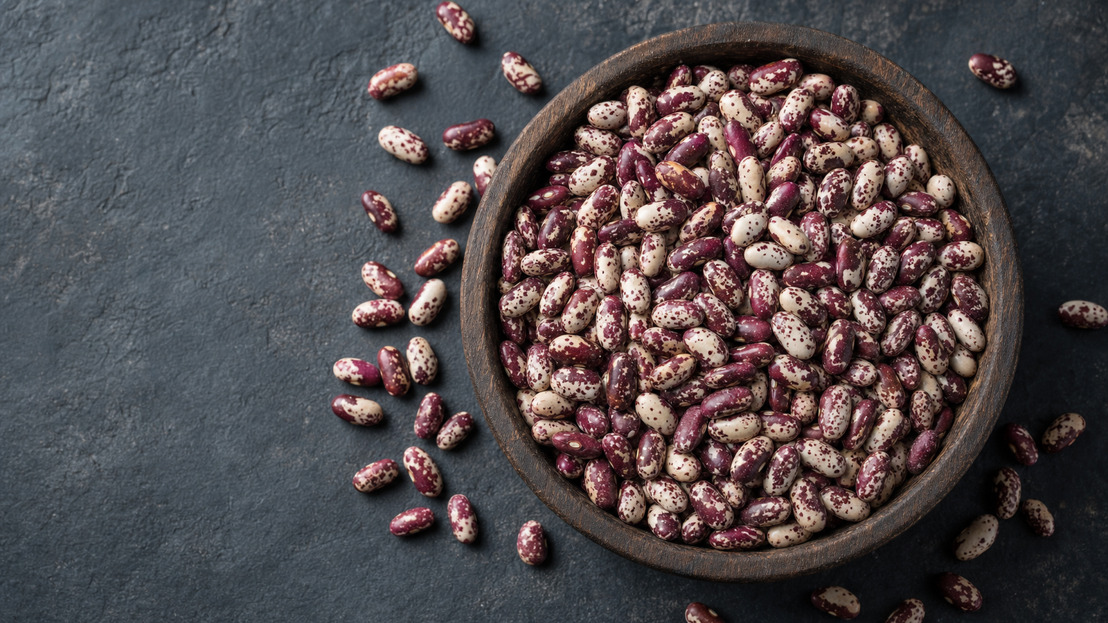 Raw Rajma Chitra (speckled cream-and-maroon kidney beans) in a rustic katori with a wooden spoon on a textured clay background